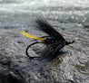 Fishing fly with black and yellow feathers on a light gray background