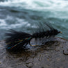 Fishing fly. Black wooly Bugger resting on a rock