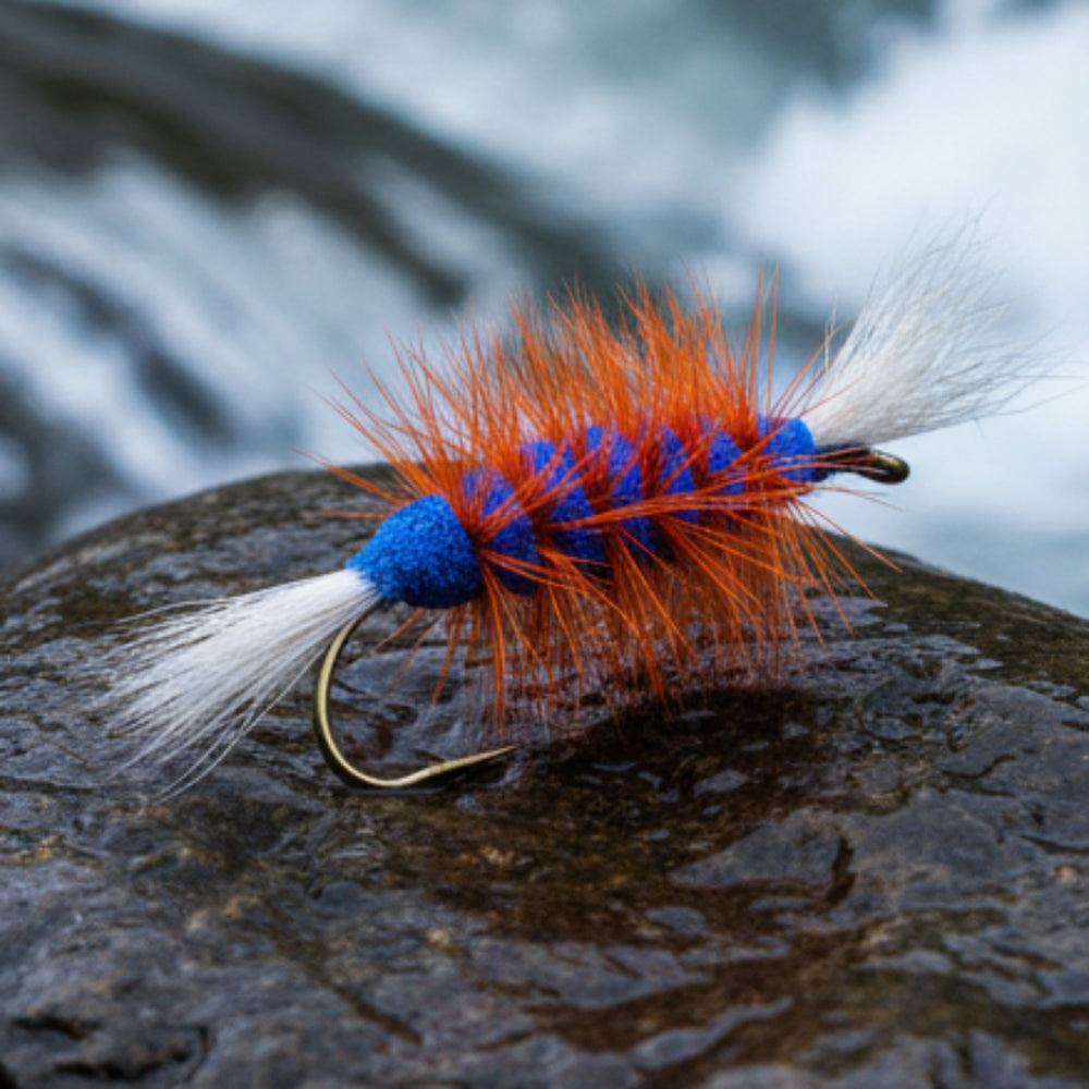 Atlantic salmon bommber fly, blue body with white tail and wing and orange hackle resting on a rock in the river