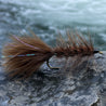 fishing fly. brown wooly bugger resting on a rock with a river in the background