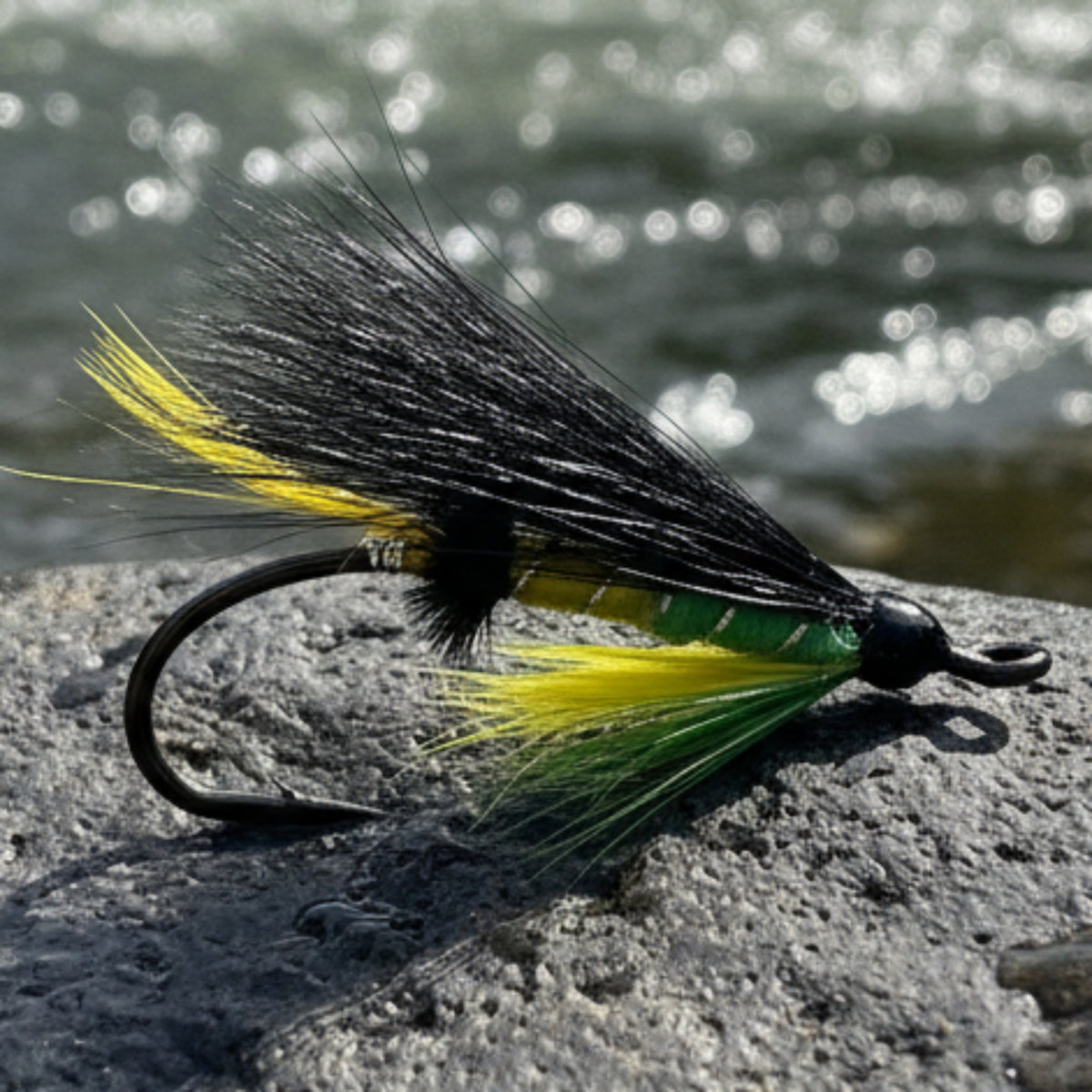 Fishing fly with black, yellow, and green feathers on a white background