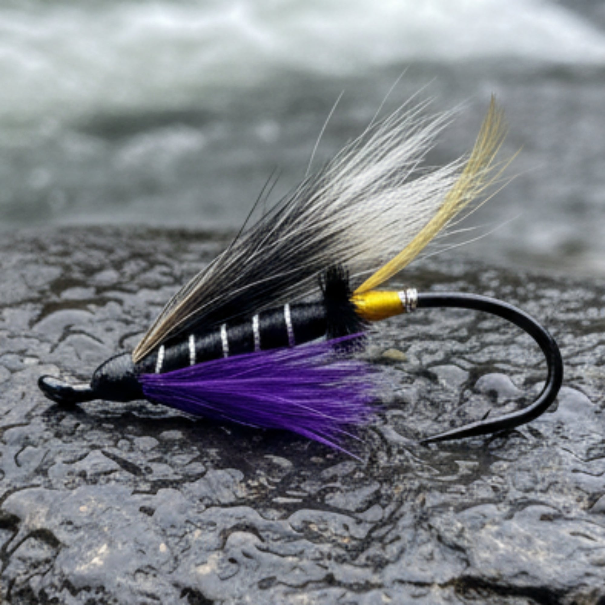 Fishing fly with black, white, and purple feathers on a light gray background
