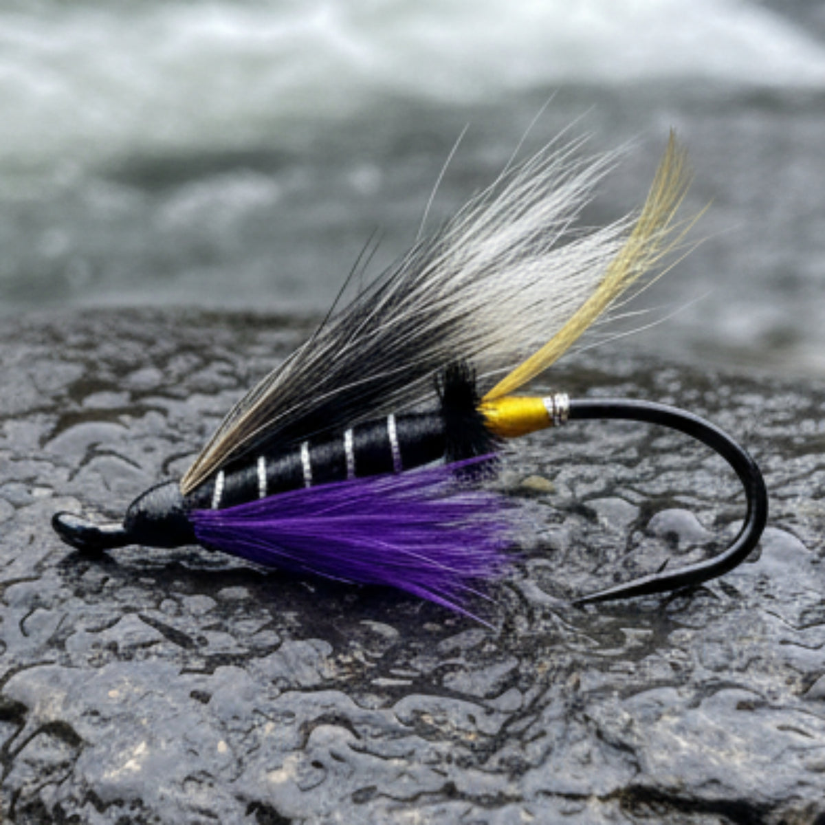 Fishing fly with black, white, and purple feathers on a light gray background