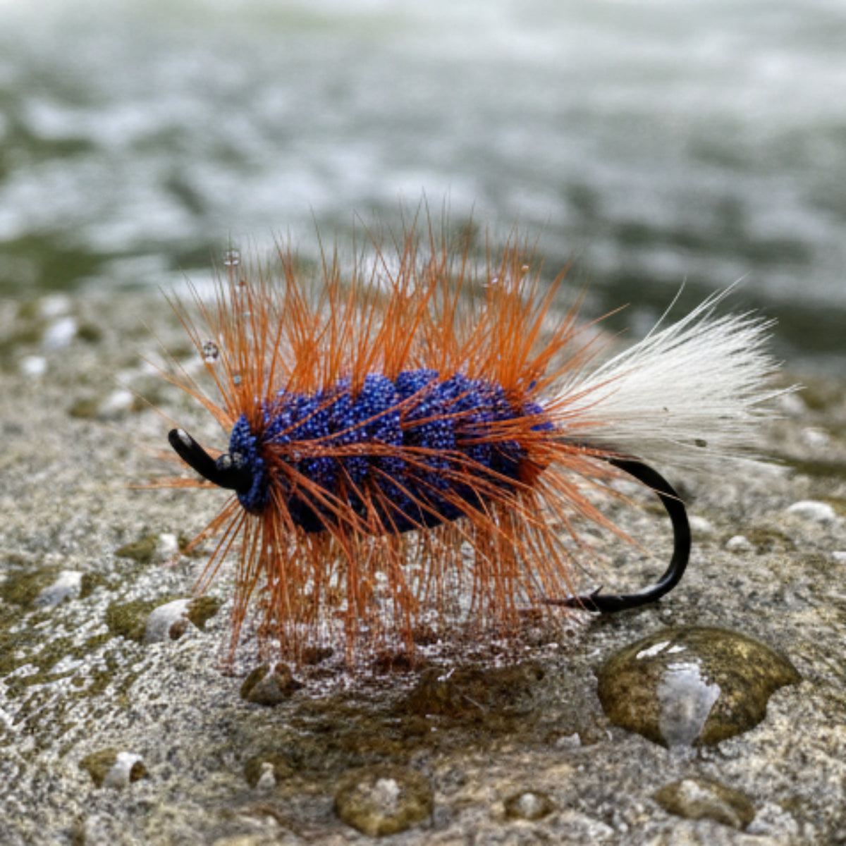 Fishing fly with orange and blue body on a white tiled background