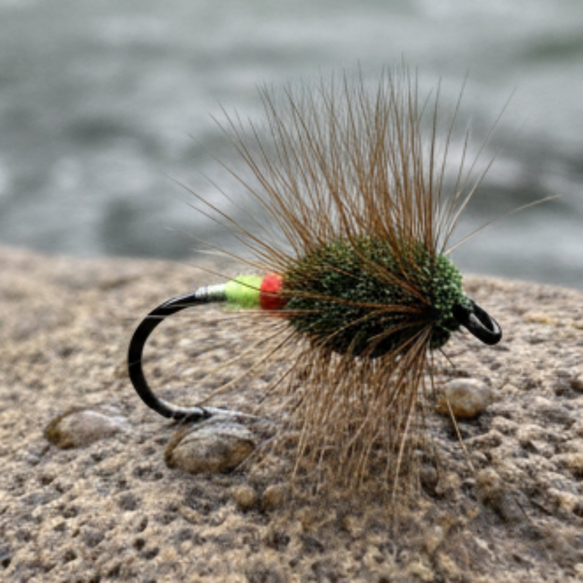 Fishing fly with brown body and green head on a white tiled background