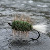 Fishing fly with green body and brown and white feathers on a tiled wall background