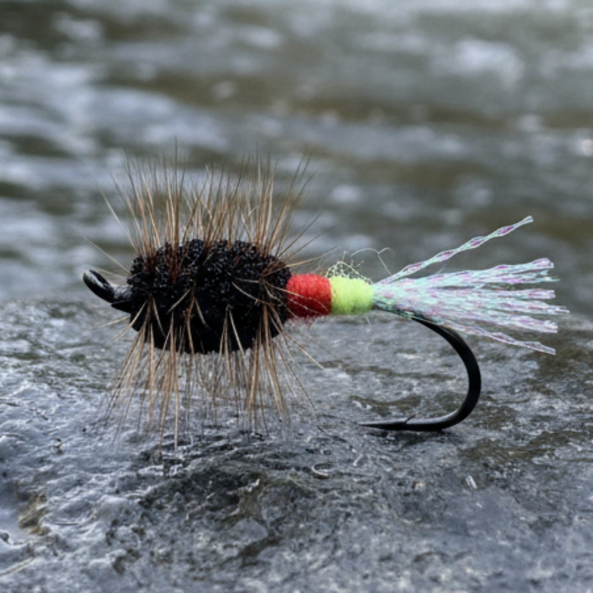 Fishing fly with black body, brown hair, red and yellow details on a white background
