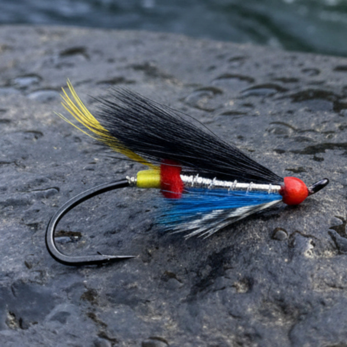 Fishing lure with black, blue, red, and yellow feathers on a light gray background