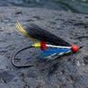 Fishing lure with black, blue, red, and yellow feathers on a light gray background