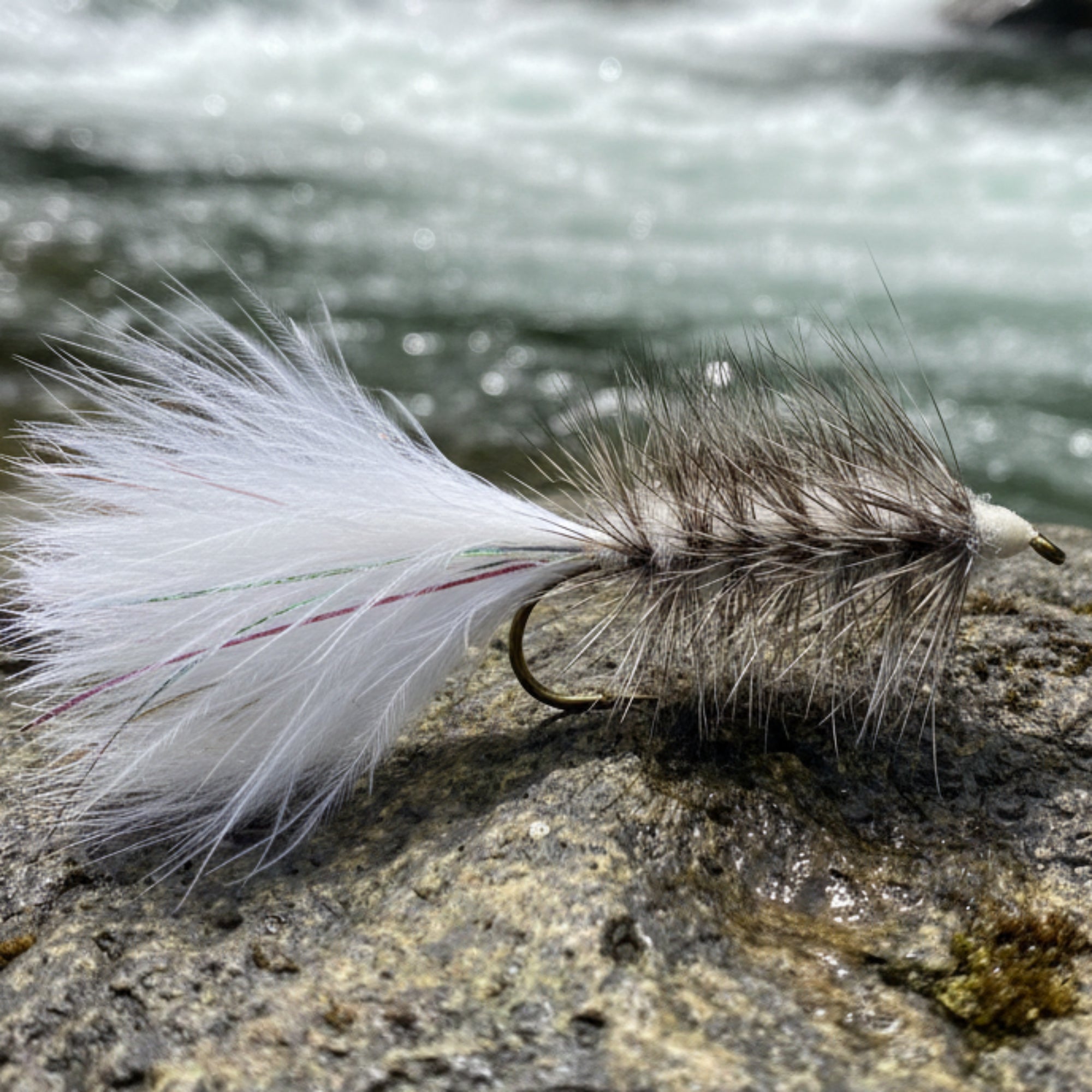 fishing fly. white wooly bugger resting on a rock next to a river
