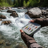 Person holding a box of colorful fishing lures with a river and rocks in the background