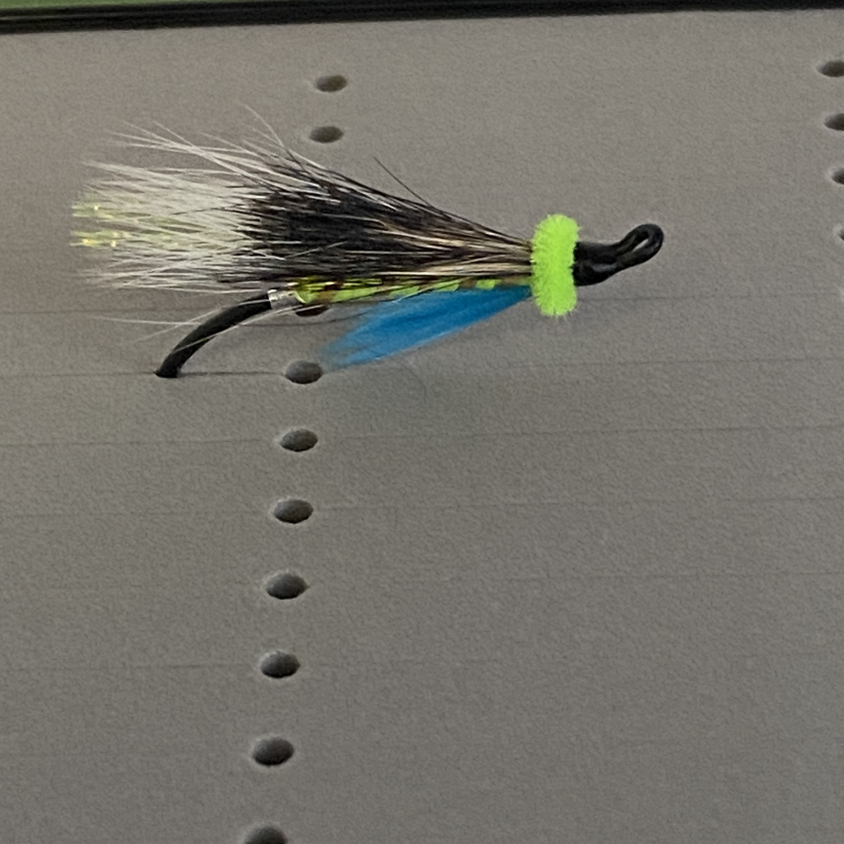Fishing fly with black, blue, and green colors on a gray surface
