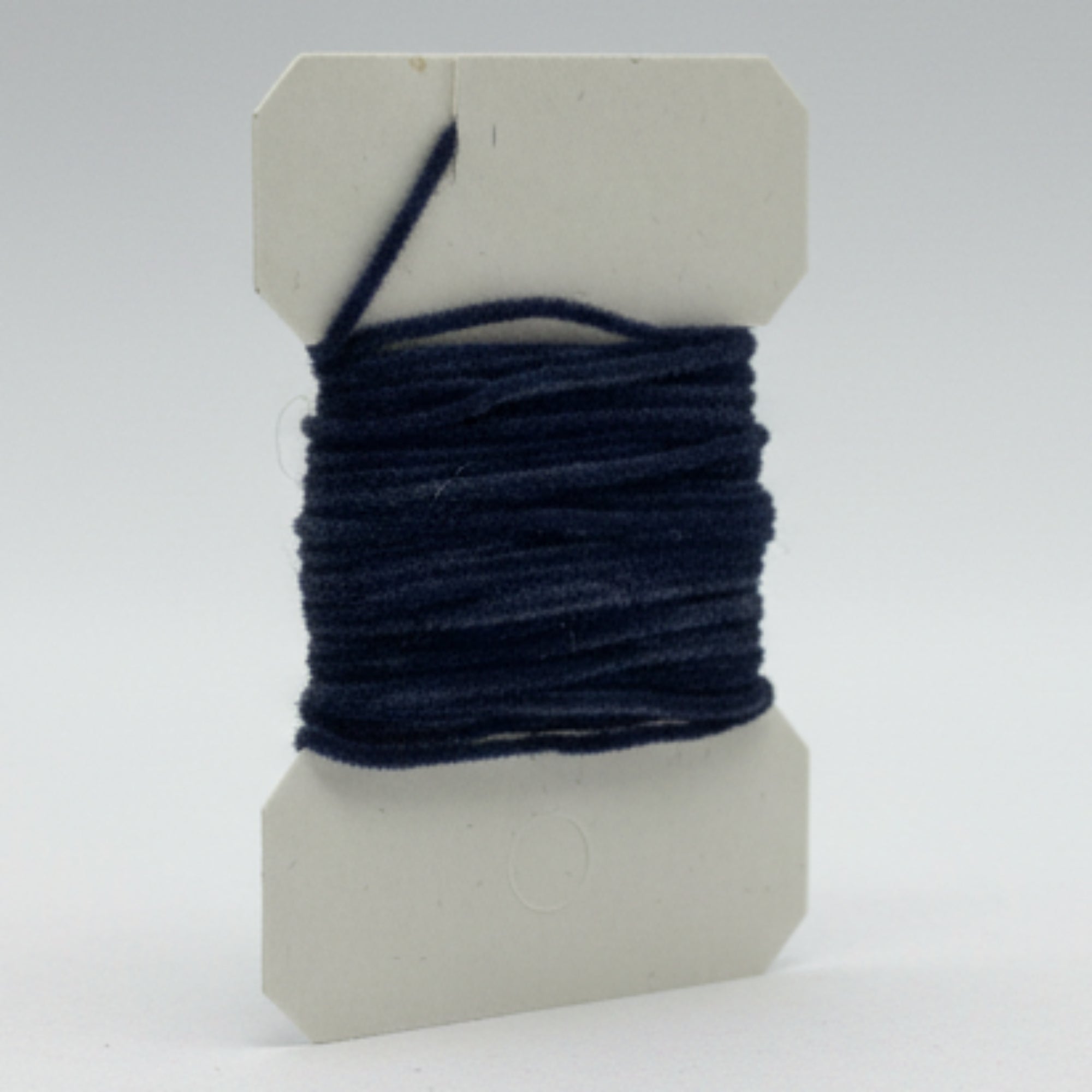 Spool of black thread on a white cardboard backing against a light gray background