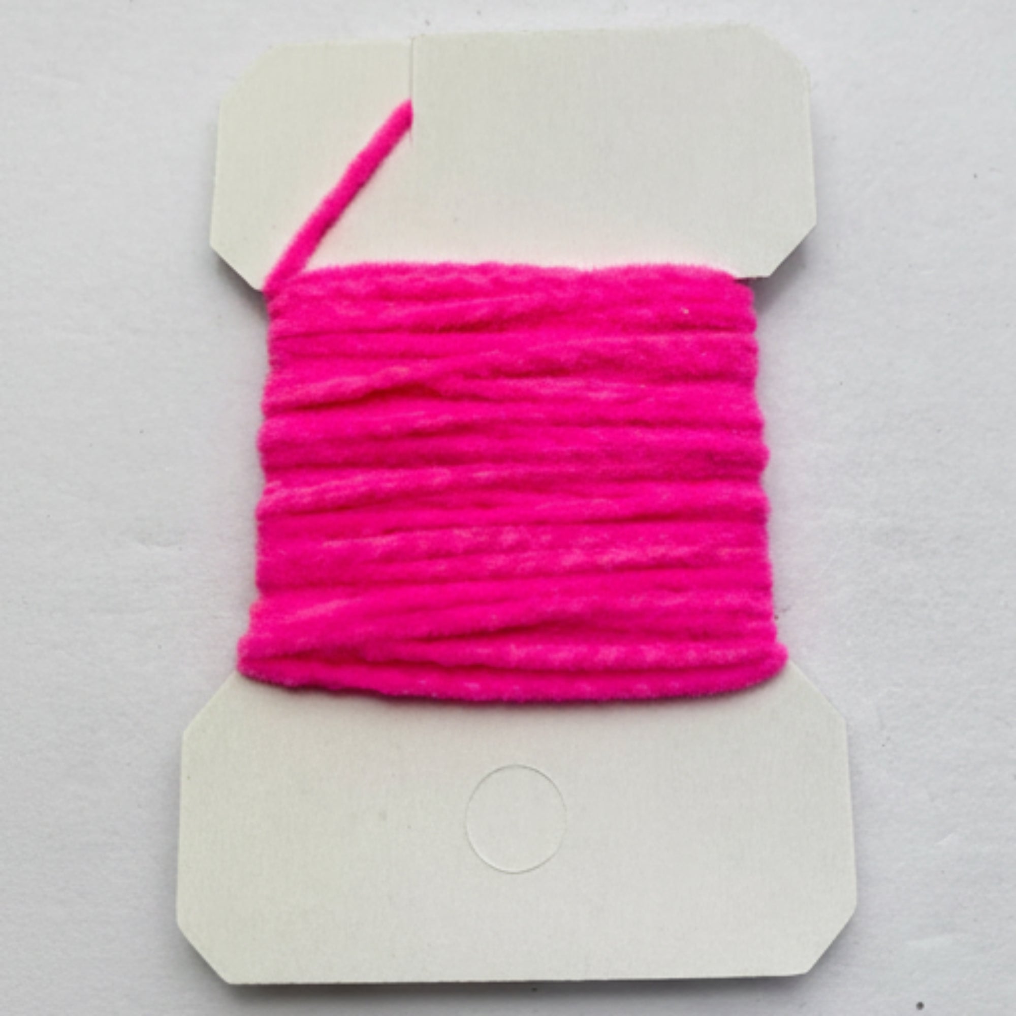 Pink yarn on a cardboard holder against a gray background