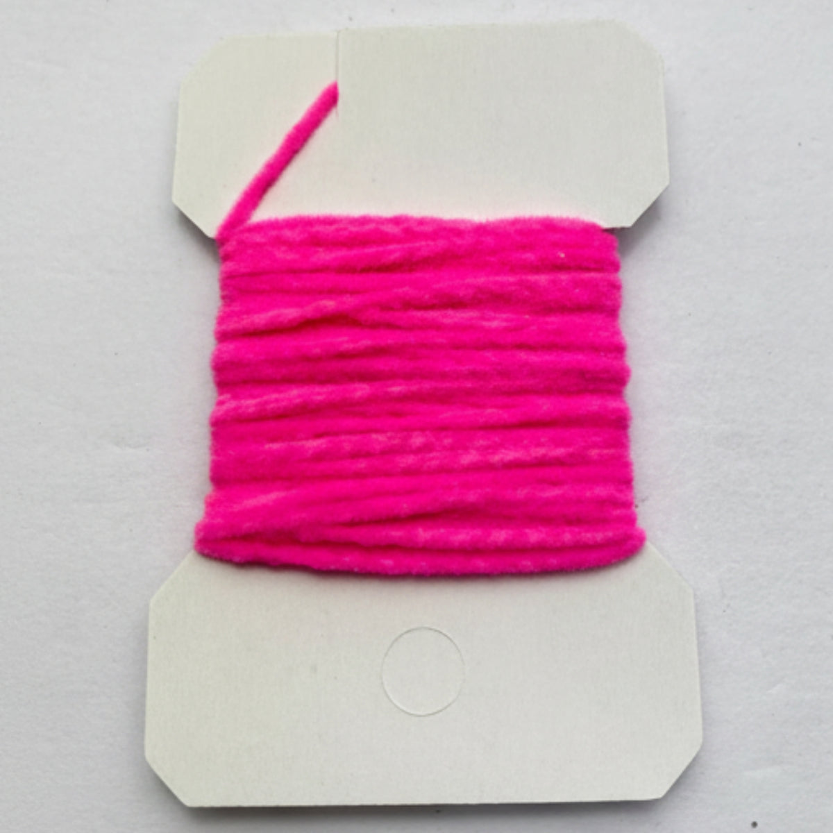 Pink yarn on a cardboard holder against a gray background