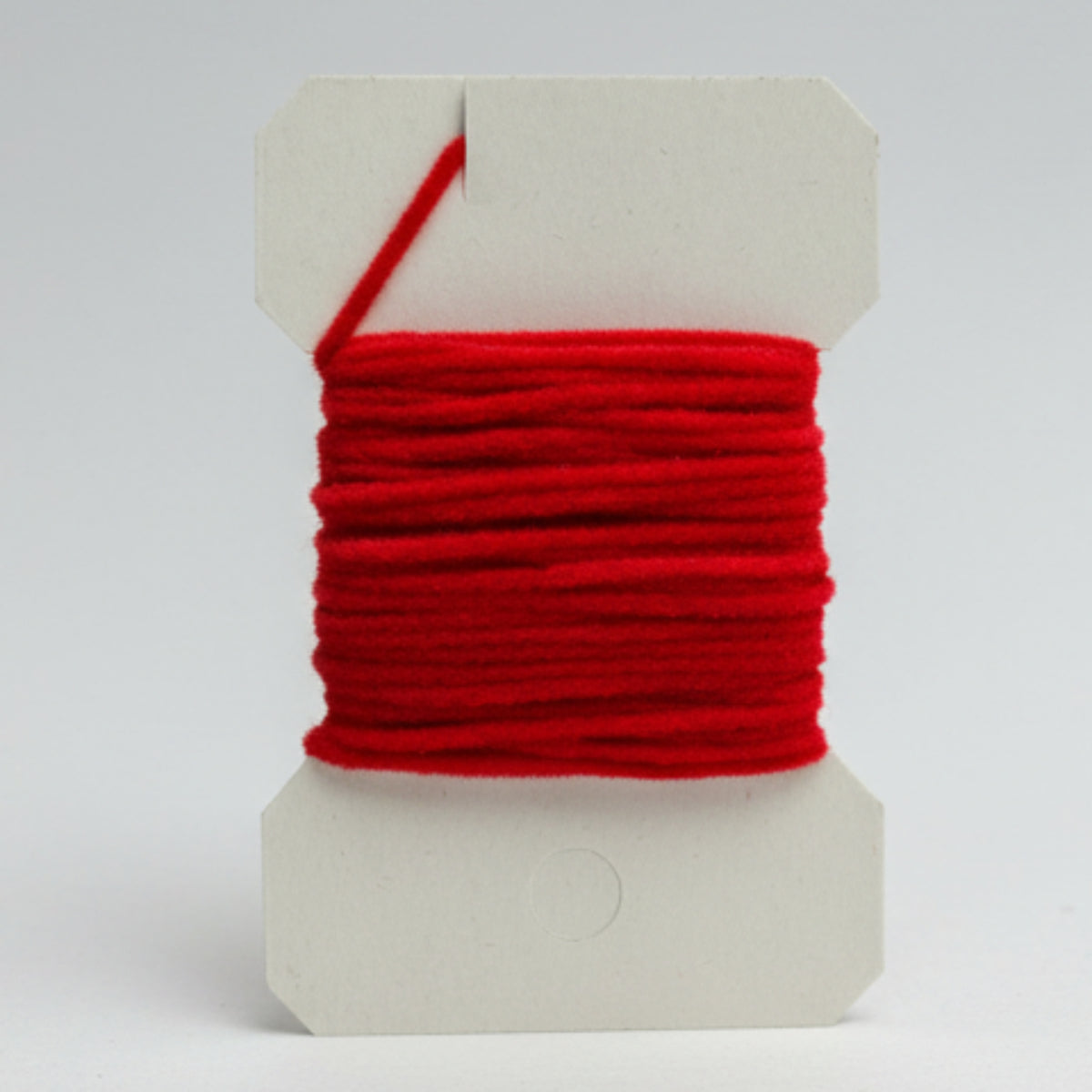 Red yarn on a white cardboard holder against a light gray background