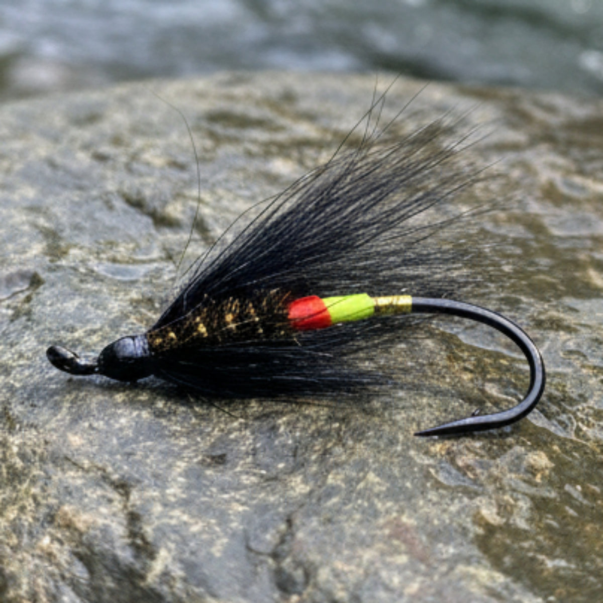 Fishing hook with black feathers and colorful bead on a light gray background