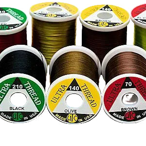 Multiple spools of UTC 140 tying thread in various colors such as black, olive, brown, and green, arranged neatly.